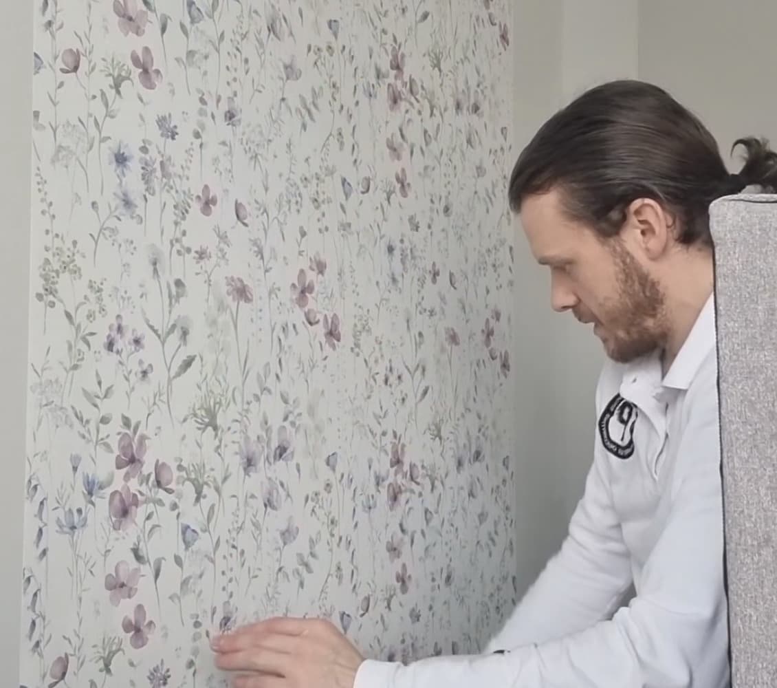 Decorator smoothing a floral wallpaper drop into place on a wall