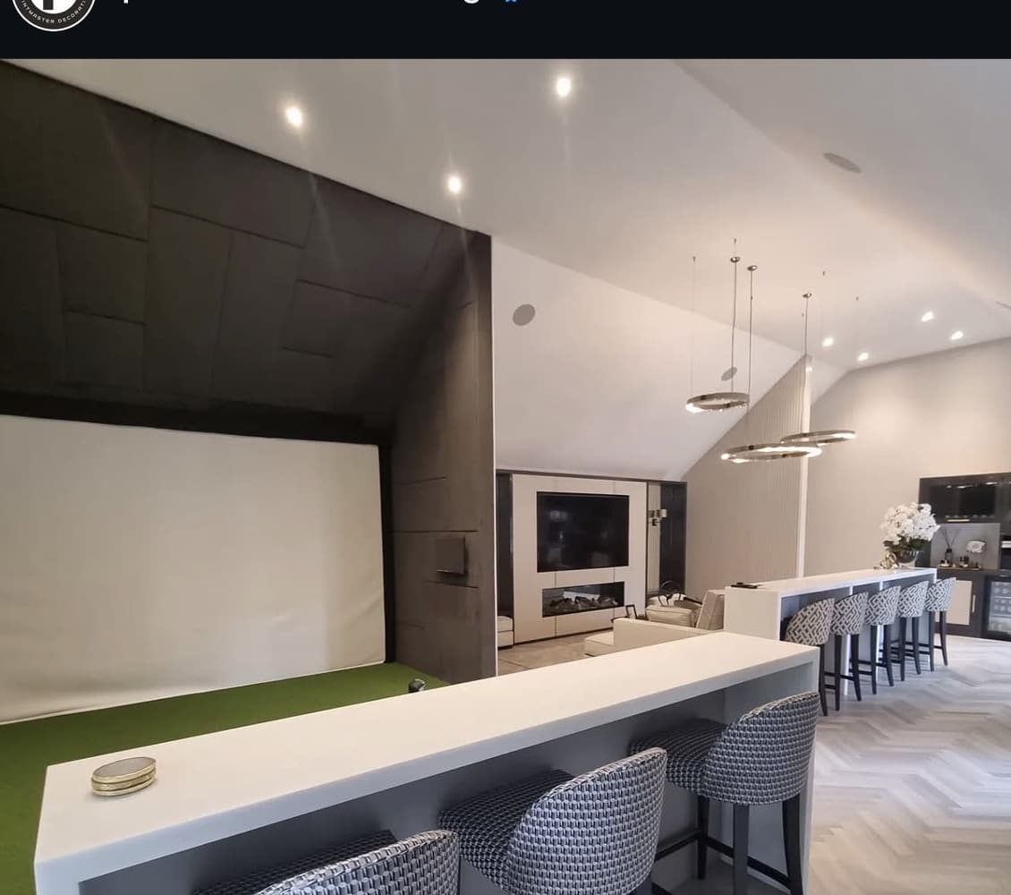Open plan kitchen and bar with a long breakfast bar, dark fitted joinery and a media wall beyond